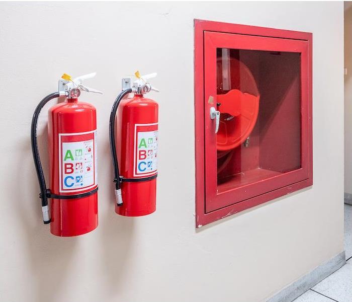 "two fire extinguisher hanging on a tan interior wall” 