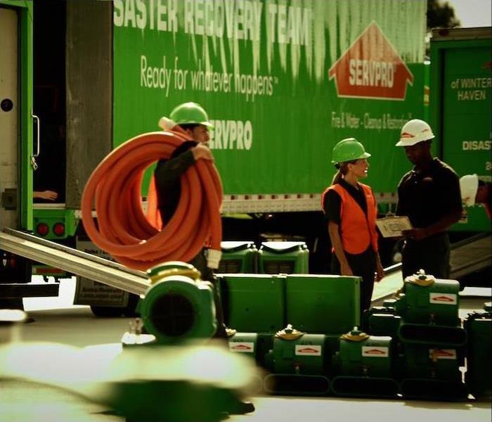 group of 3 SERVPRO reps standing near a green semi truck at a work site